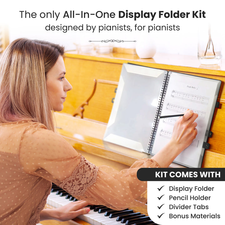 Woman seated at a piano, writing directly onto sheet music held in an open display folder with divider tabs. The folder lies flat, making it easy to take notes. The title reads, 'The only all-in-one display folder kit designed by pianists, for pianists
